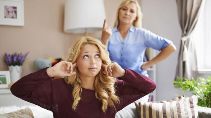 Prkosna tinejdžerka pokriva uši prstima u sobi dok ju majka grli