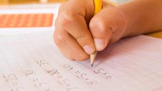 Djetetova ruka koja ispunjava domaći zadatak uz pomoć matematičkog smještaja